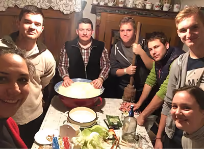 Hét ember egy asztal körül, étellel és konyhai eszközökkel egy hangulatos szobában.